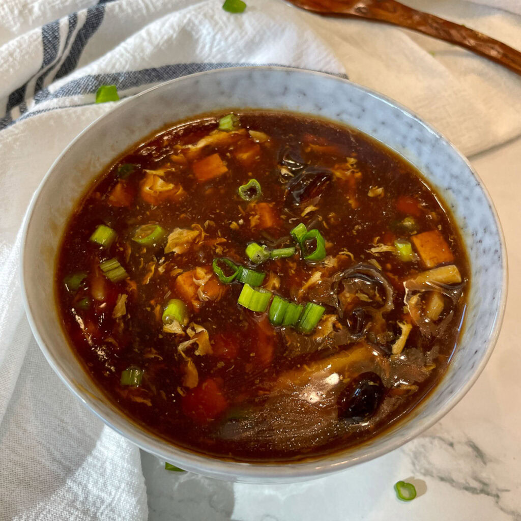 Bowl of hot and sour soup with tofu, mushrooms and green onions