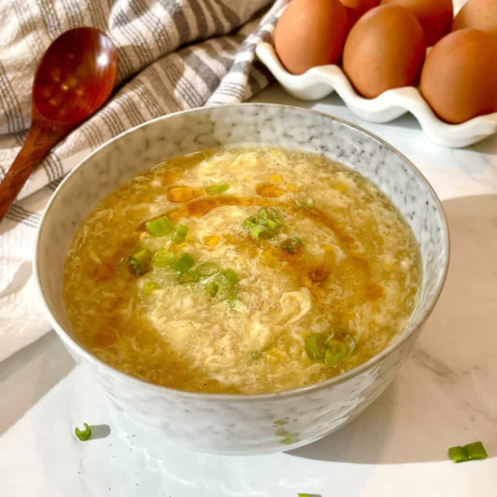 Bowl of corn egg drop soup with silky egg ribbons, sweet corn and green onions