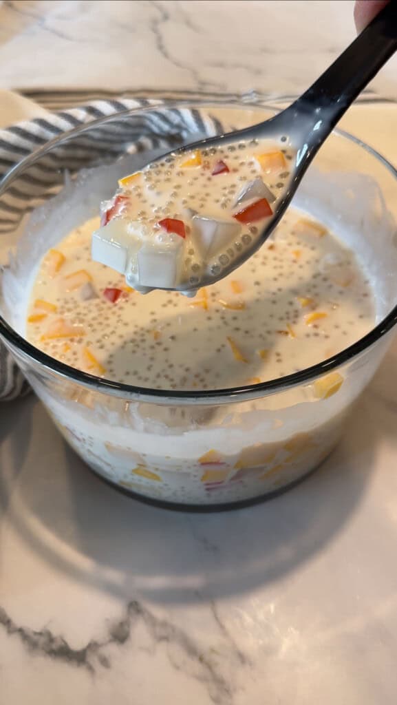 Spoonful of creamy mango sago with sago pearls, mango and nata de coco coconut jelly over a glass bowl