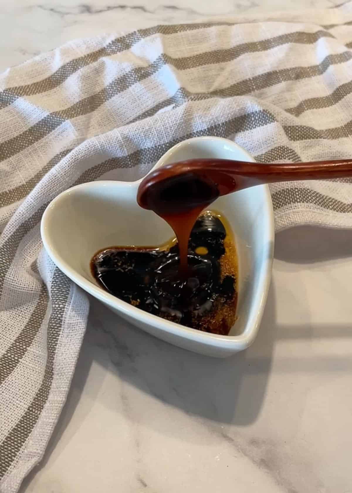 A brown wooden spoon scooping sauce into a heart-shaped bowl