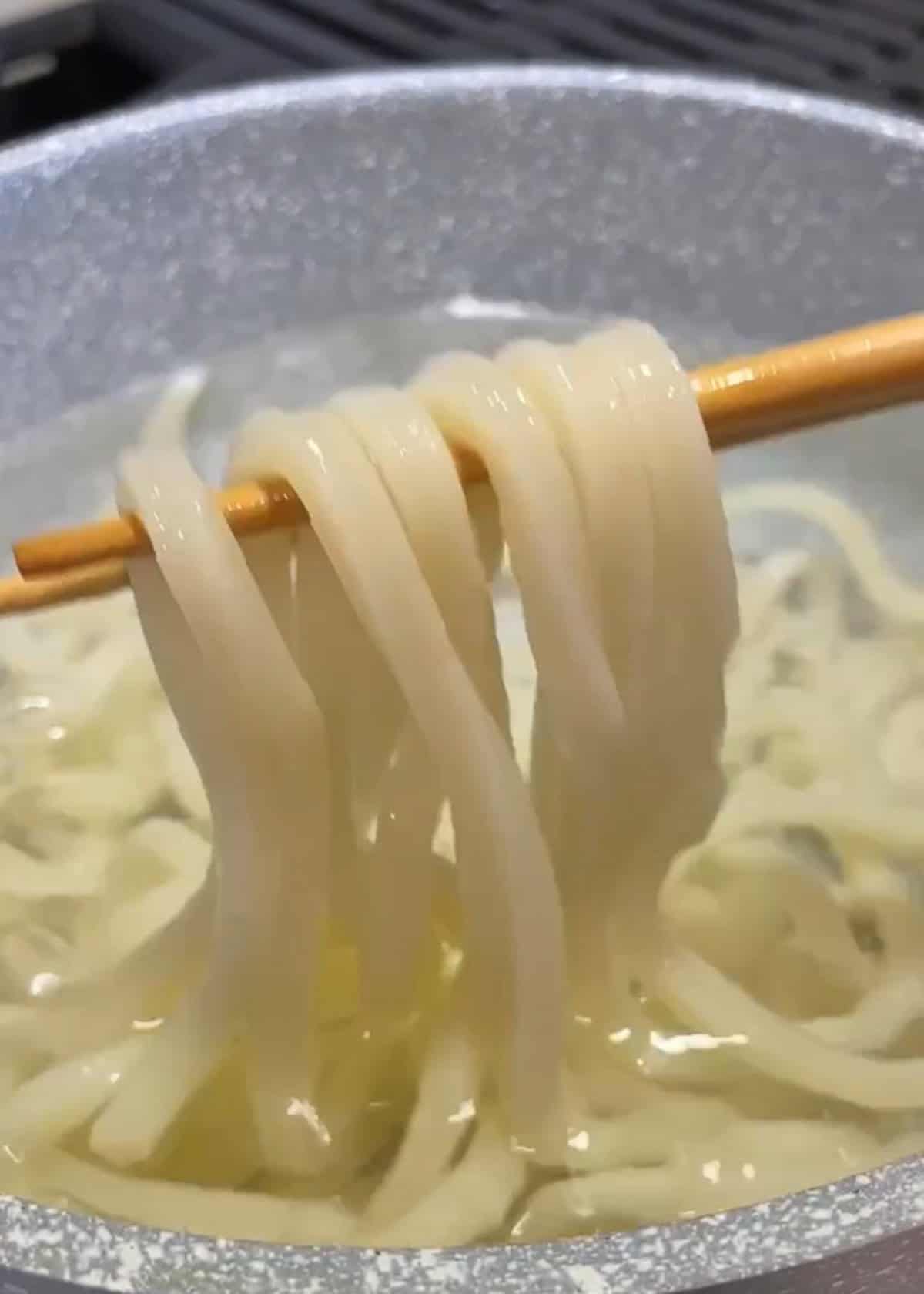A brown chopstick holding up noodles in a pot