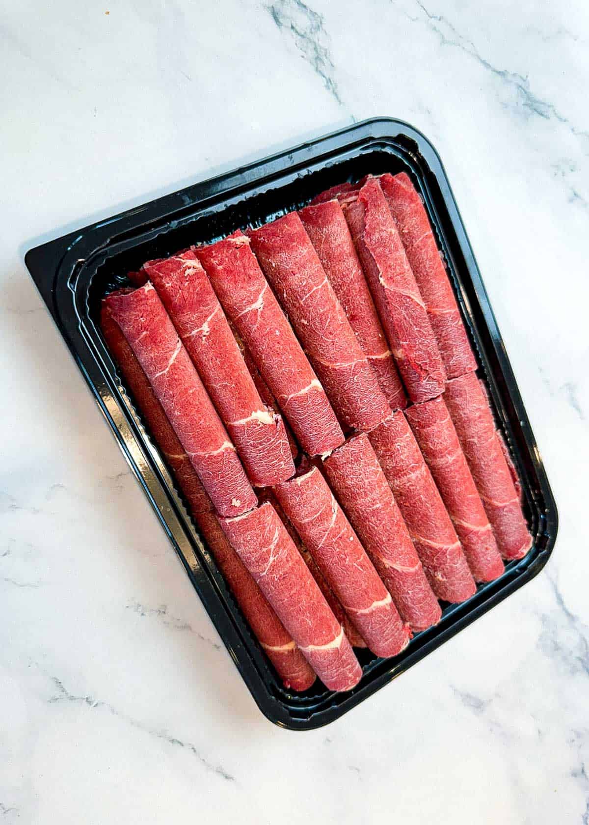 Sliced beef Rolls on a black platter on a marble surface.
