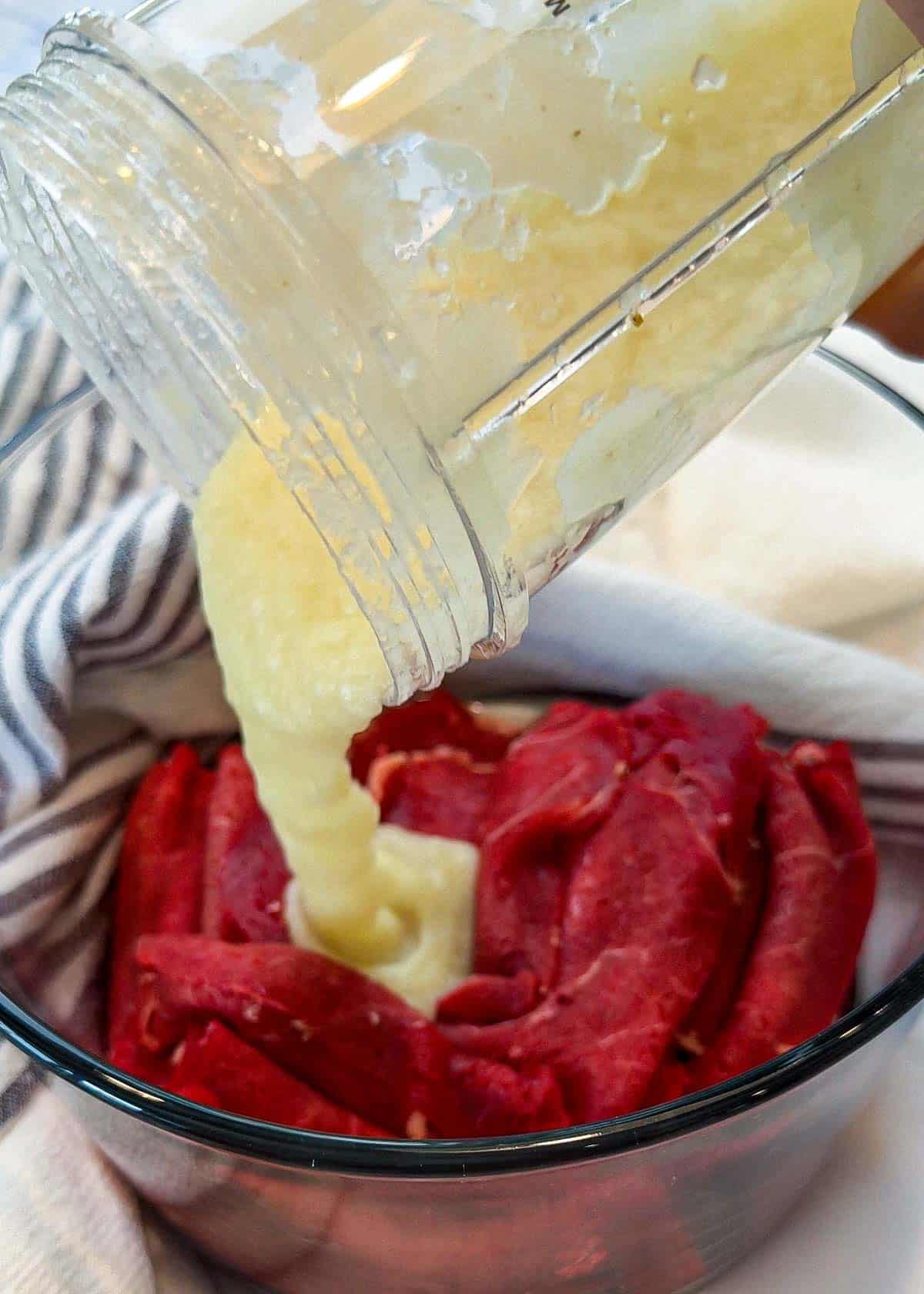 Pouring blended marinating and ingredients over sliced beef.