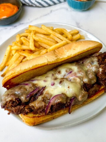 Plated Bulgogi Beef Cheesesteak sandwich on a white plate with fries
