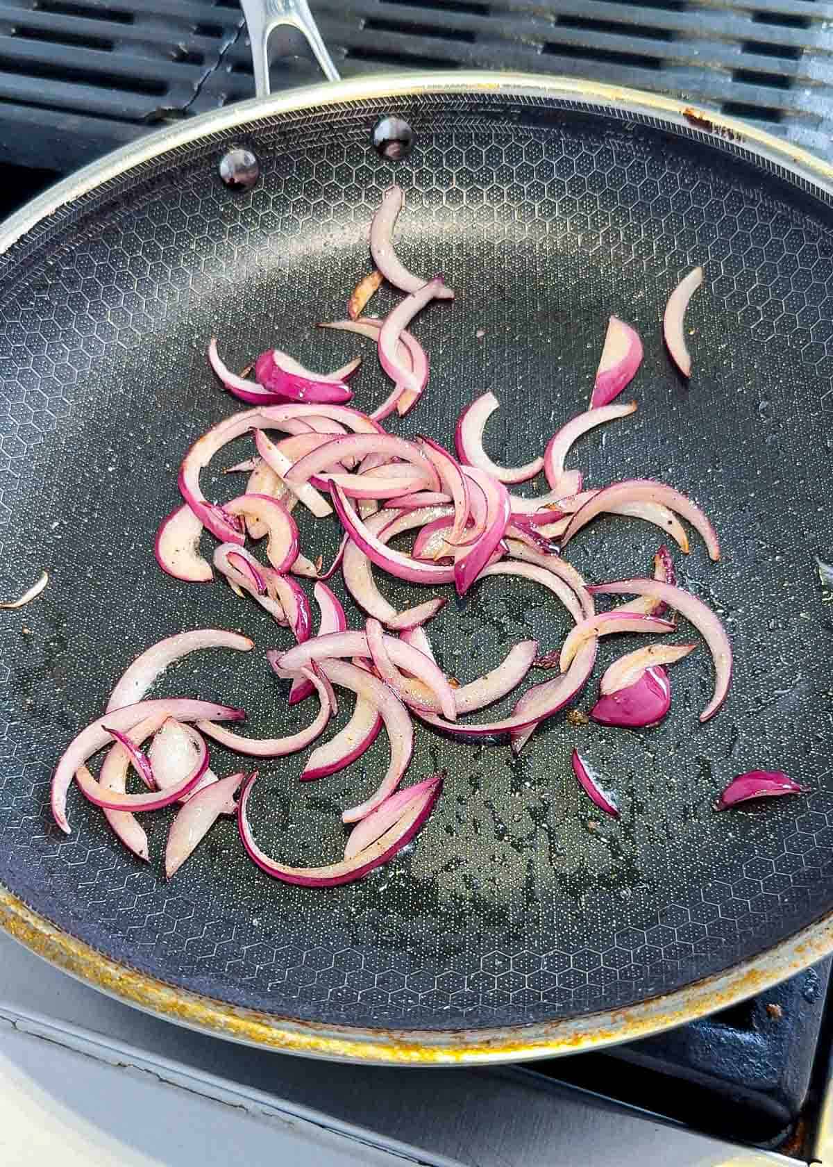 Sautรฉ red onions in a black pan