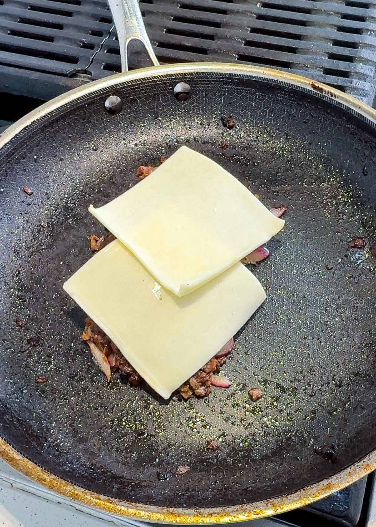 Sliced beef with onions for cheese steak with two slices of cheese on top