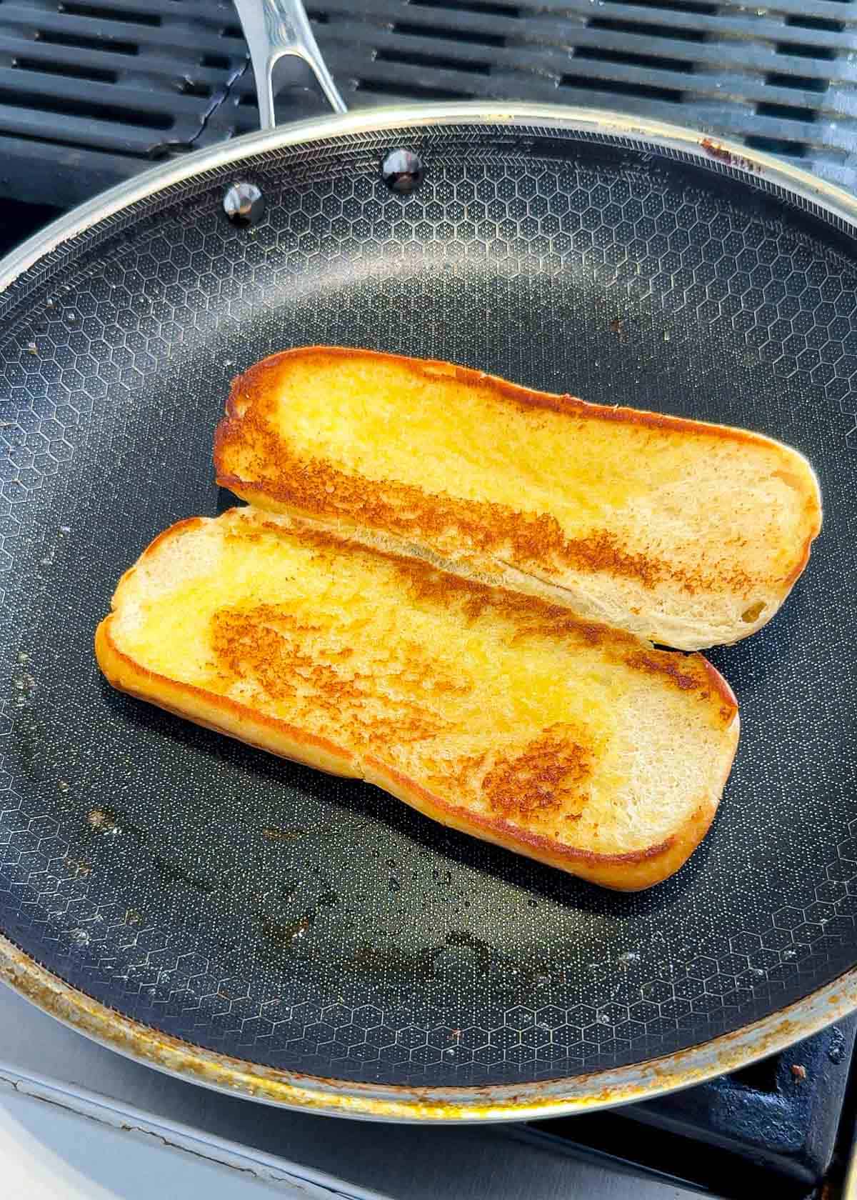 Toasted hoagie roll with butter on both sides in a black pan