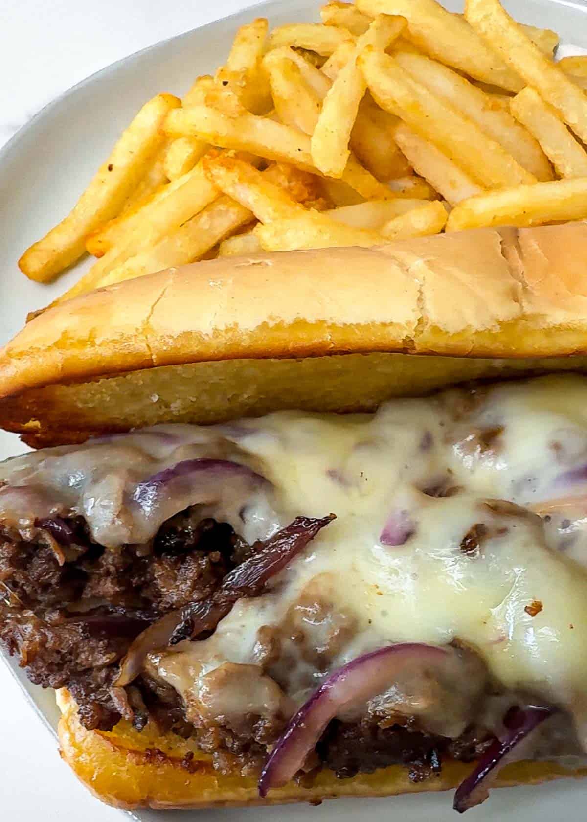 a close-up of a bulgogi cheese steak with melted cheese on top in a toasted hoagie roll on a white plate with fries.