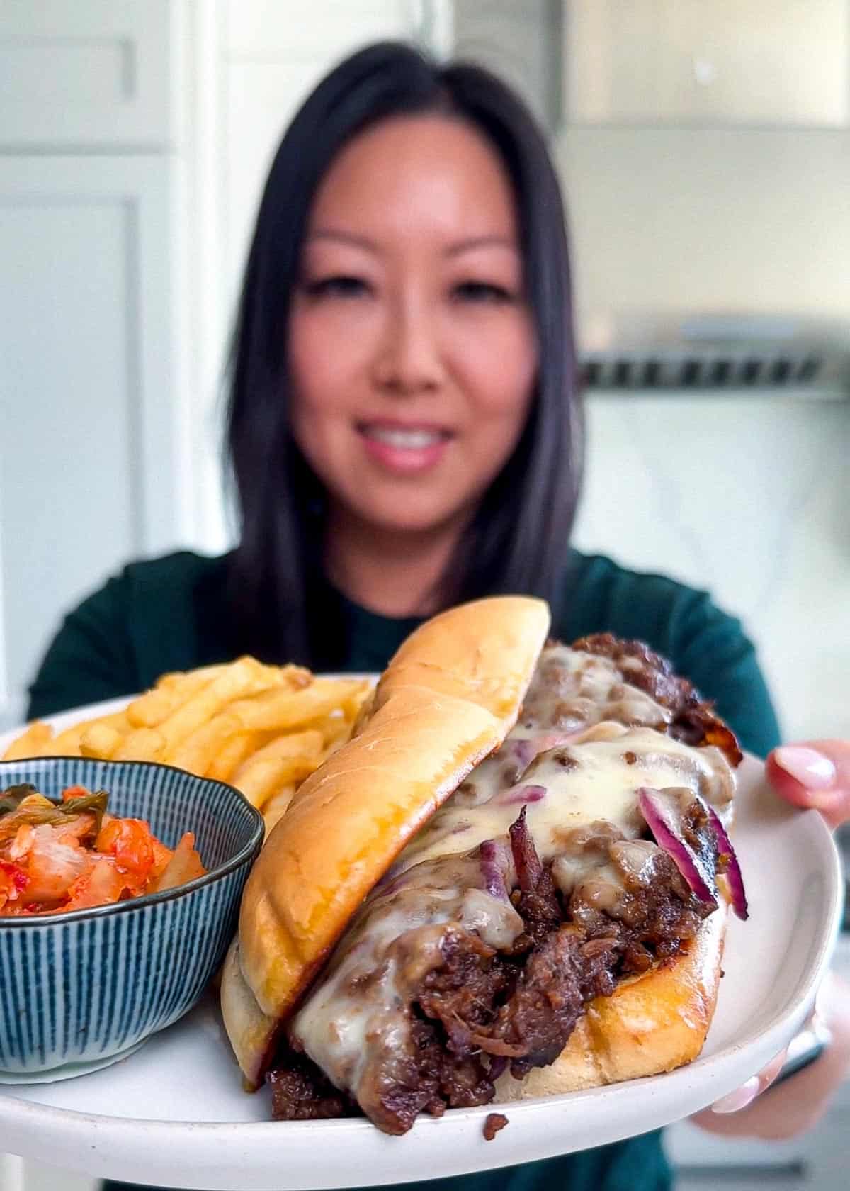 thesavorychopstick holding Plated Bulgogi Cheesesteak with fries