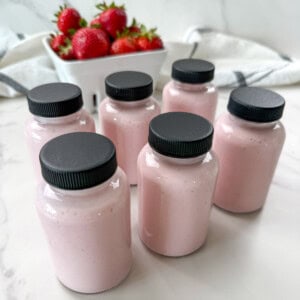 home made yogurt drinks in glass jars with a basket of strawberries.