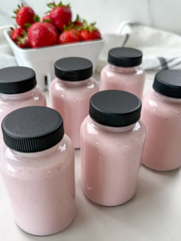 home made yogurt drinks in glass jars with a basket of strawberries.