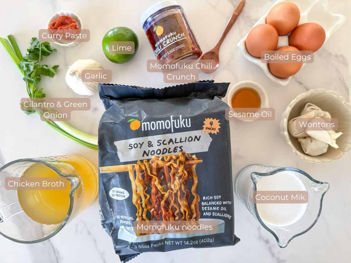 All ingredients for curry noodle soup including Momofuku noodles, red curry paste, chili crisp, coconut milk, chicken broth, dumplings, garlic, green onions, and optional toppings
