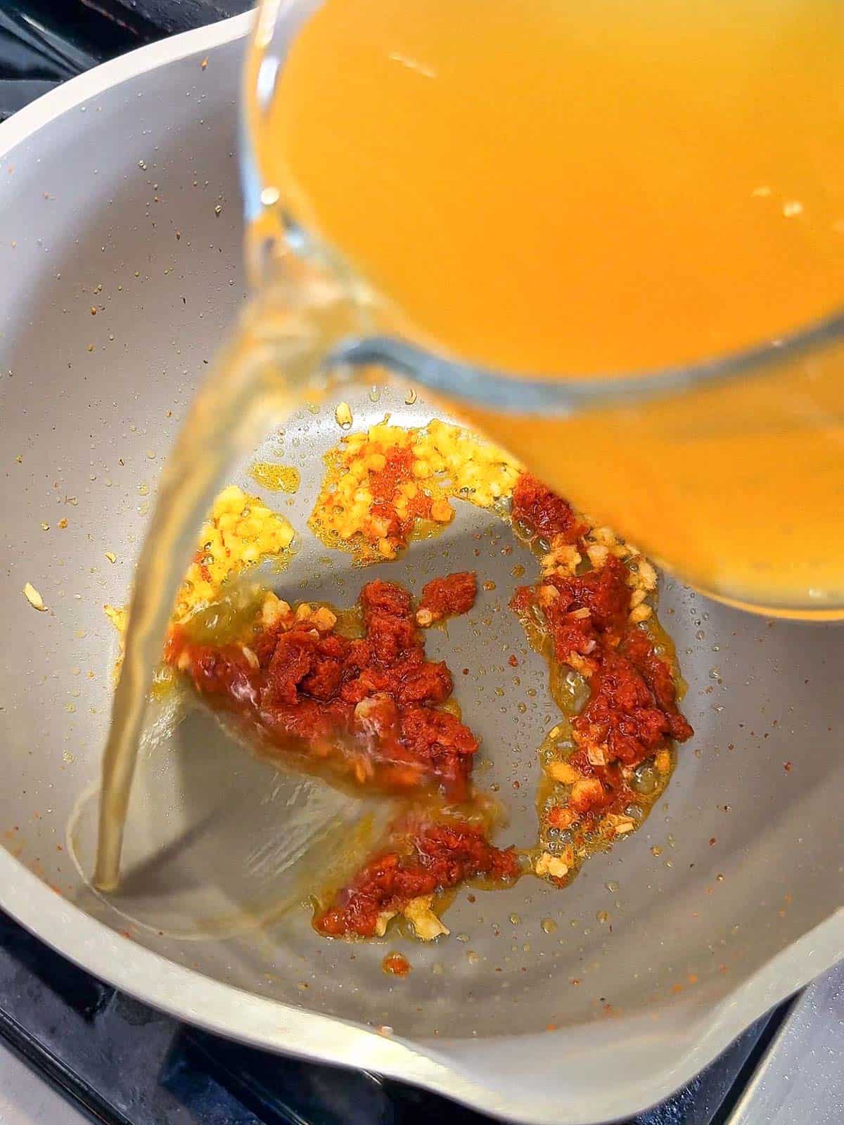 Pot of chicken broth and coconut milk being stirred for curry noodle soup