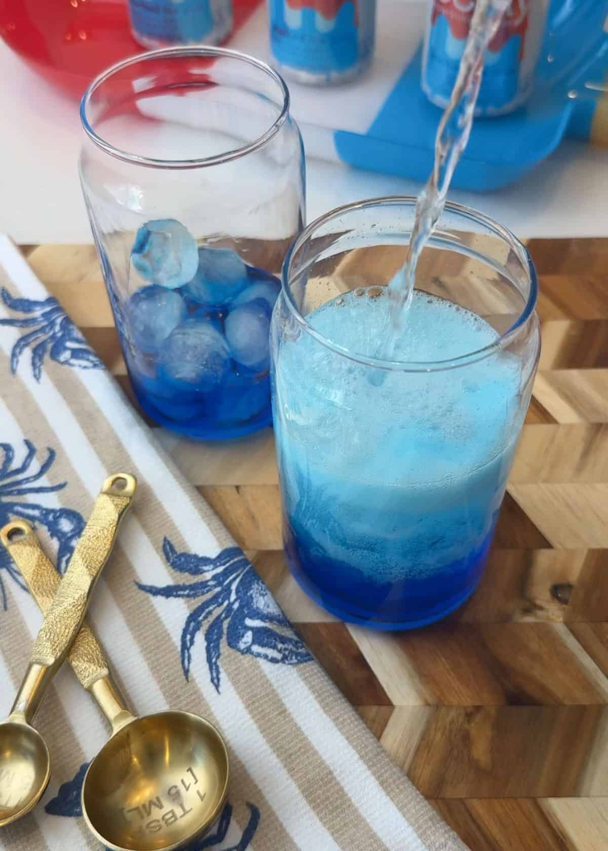 Clear glass cups with Blue liquid inside and clear liquid getting poured in