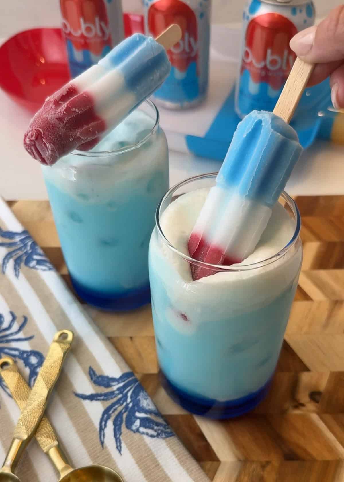 Red white and blue popsicle on a creamy blue and white drink in a clear cup