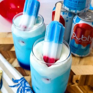 Blue drink and a glass cup with white foam and two rocket shaped popsicles that are red white and blue