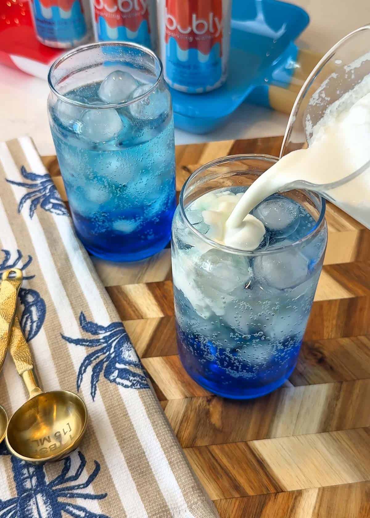 White liquid being poured into a clear glass with blue liquid inside