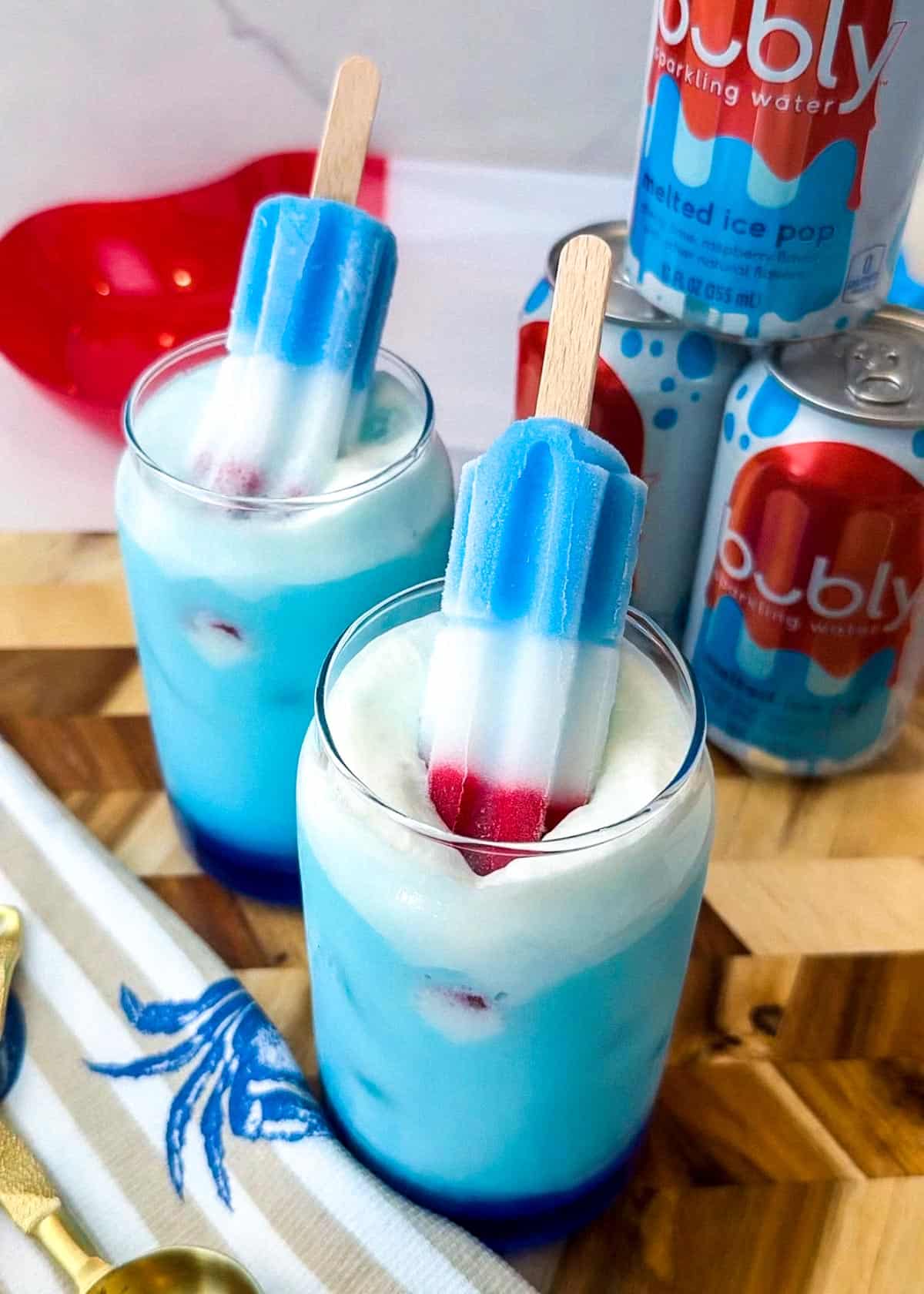 Blue drink and a glass cup with white foam and two rocket shaped popsicles that are red white and blue