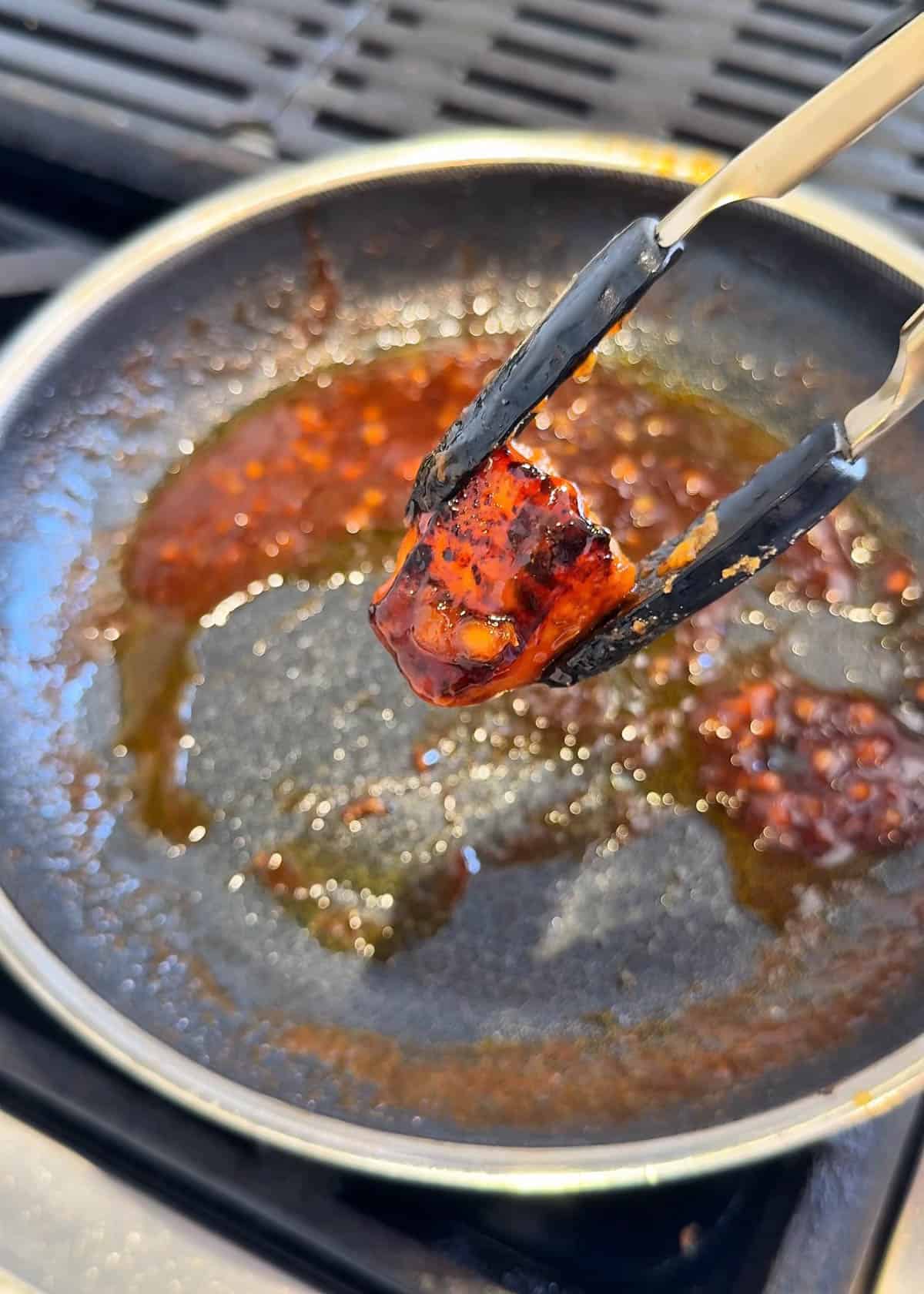 Glazed cubed salmon held up with tongs over a pan