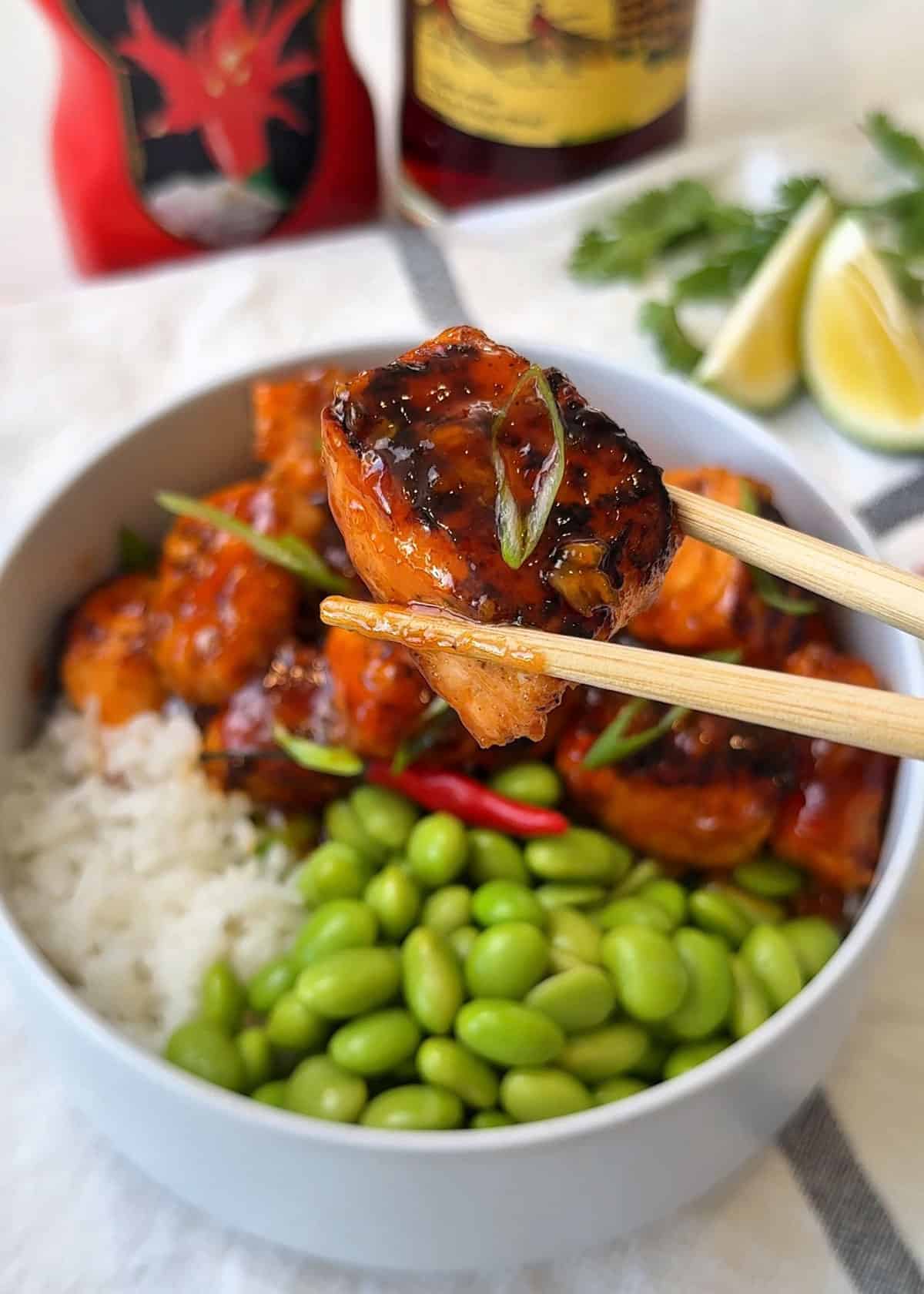 Beautifully glazed salmon held in a chopstick or a bowl of rice and edamame