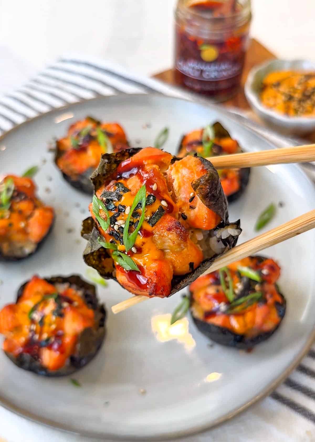 Baked salmon wrapped in seaweed held by wooden chopsticks over a plate
