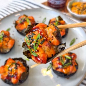 Baked salmon wrapped in seaweed held by wooden chopsticks over a plate