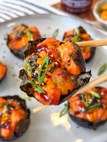 Baked salmon wrapped in seaweed held by wooden chopsticks over a plate