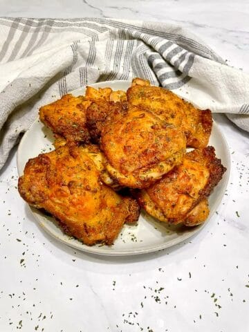 Plate of golden, crispy bone-in air fryer chicken thighs on a marble counter