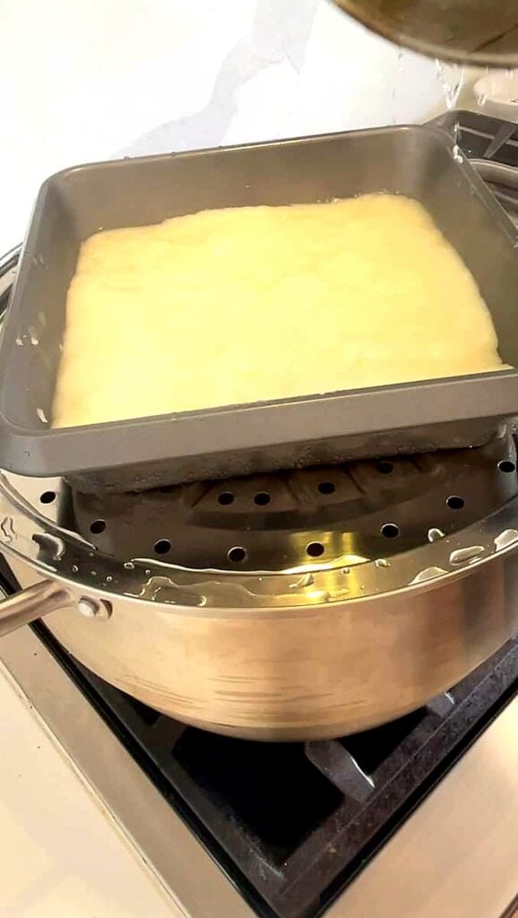 Steamed rice cake in a square pan sitting on top of a steamer
