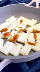 Sliced rice cakes frying in a skillet with oyster sauce drizzled on top