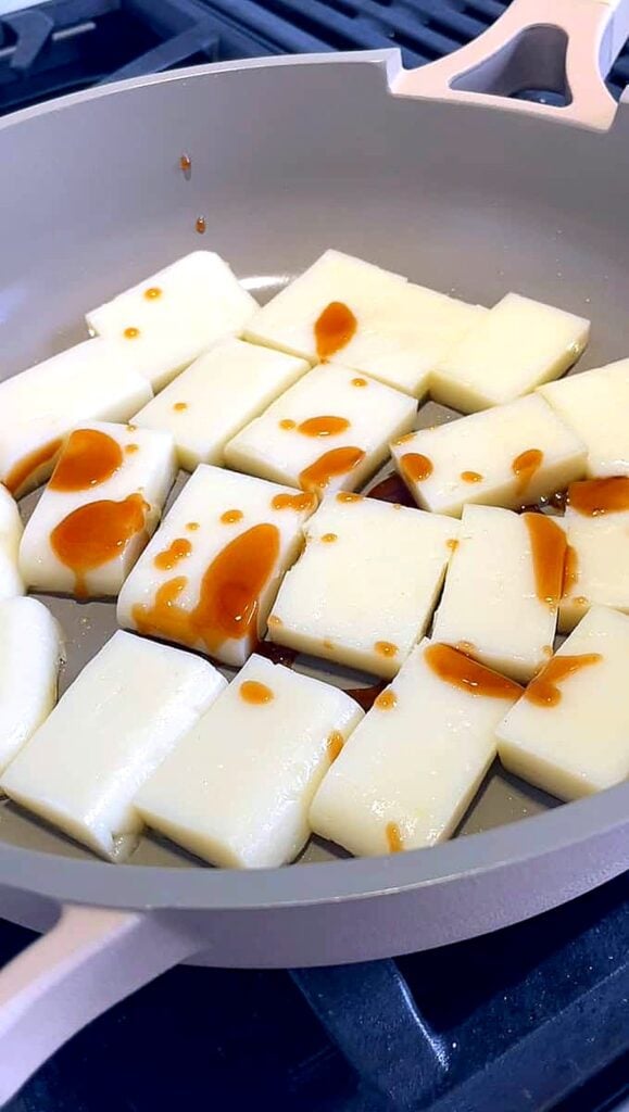 Sliced rice cakes frying in a skillet with oyster sauce drizzled on top