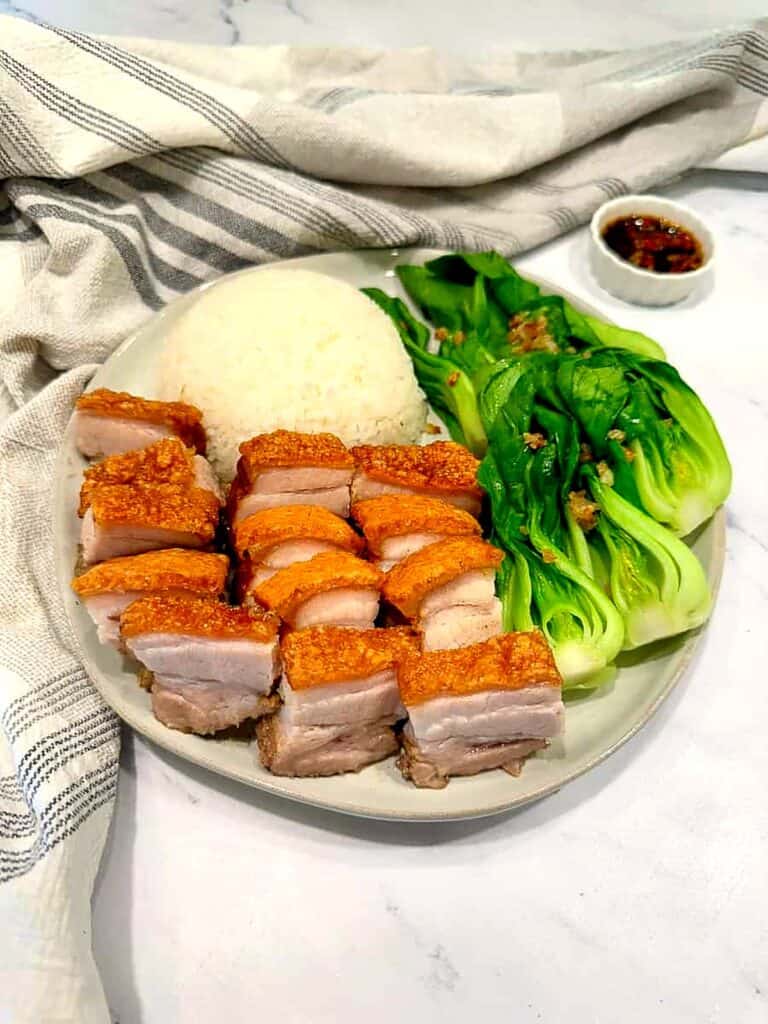Crispy Chinese roast pork belly slices with crackling skin served with white rice and bok choy