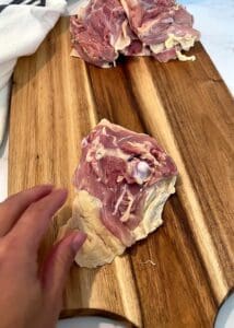 Raw bone-in chicken thigh placed skin side down on a cutting board with the bone showing