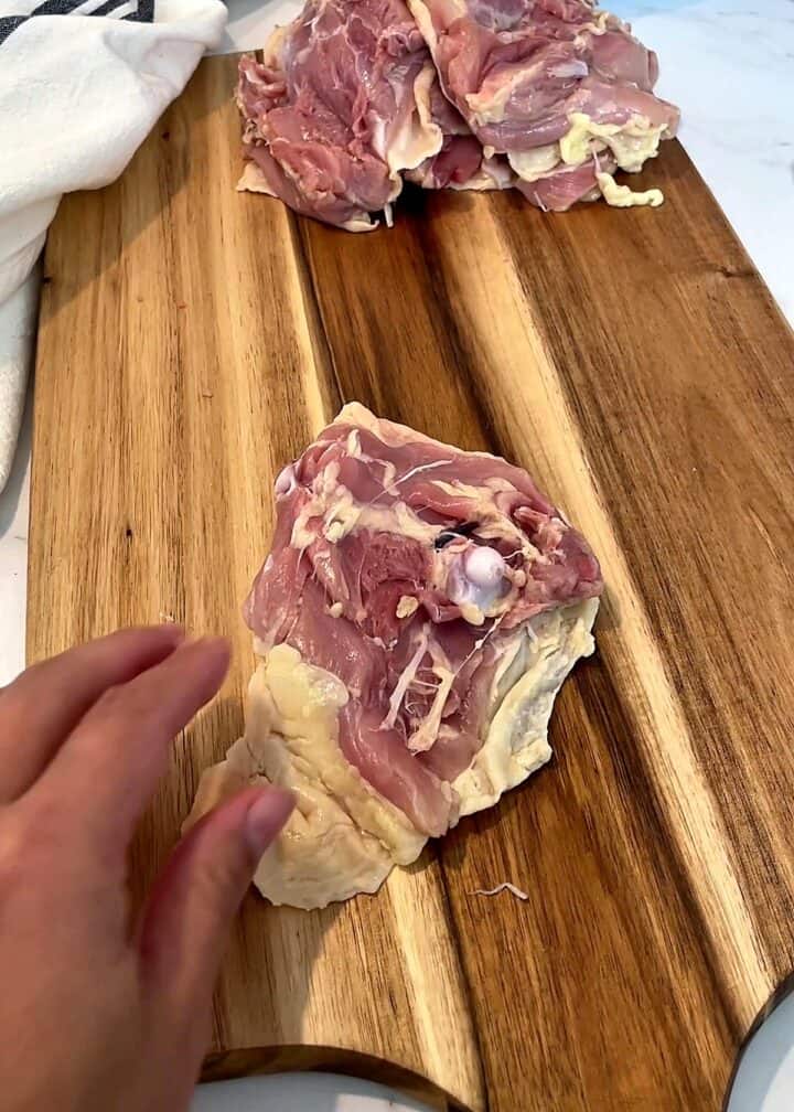 Raw bone-in chicken thigh placed skin side down on a cutting board with the bone showing