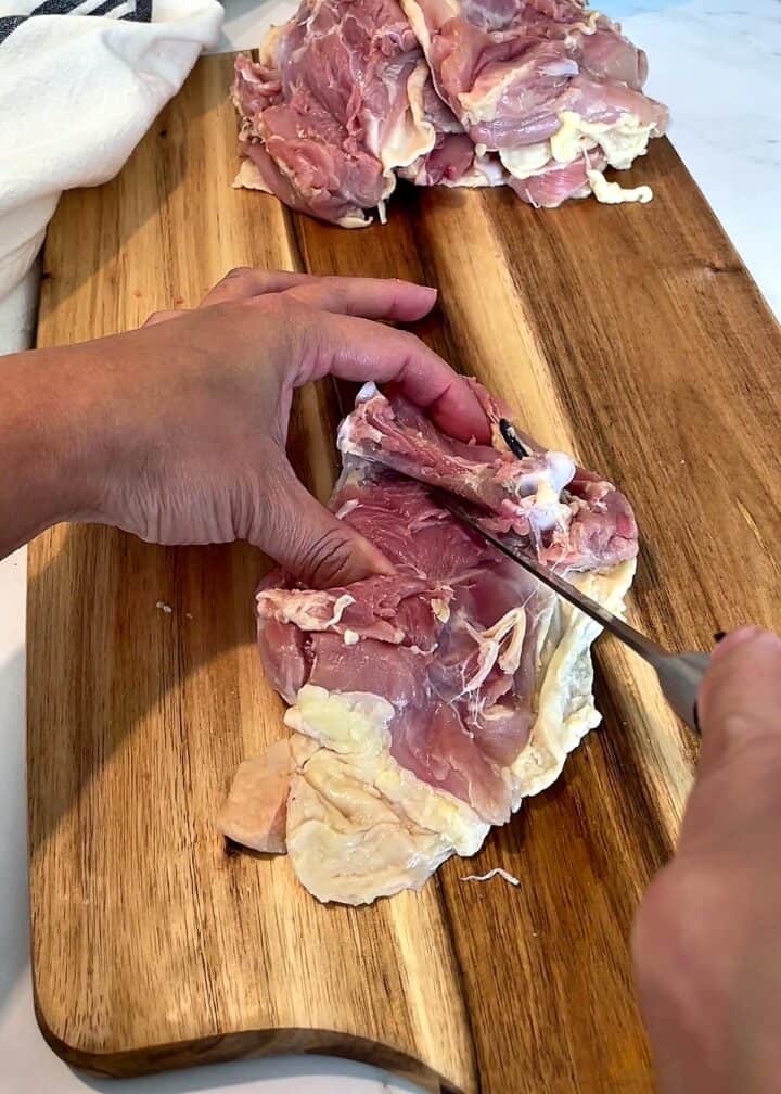 Opening up a chicken thigh and cutting the meat away from both sides of the bone