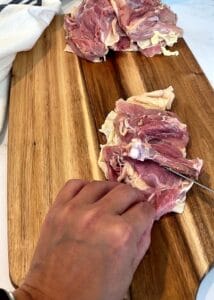 Sliding the knife tip under the chicken thigh bone to free it from the meat