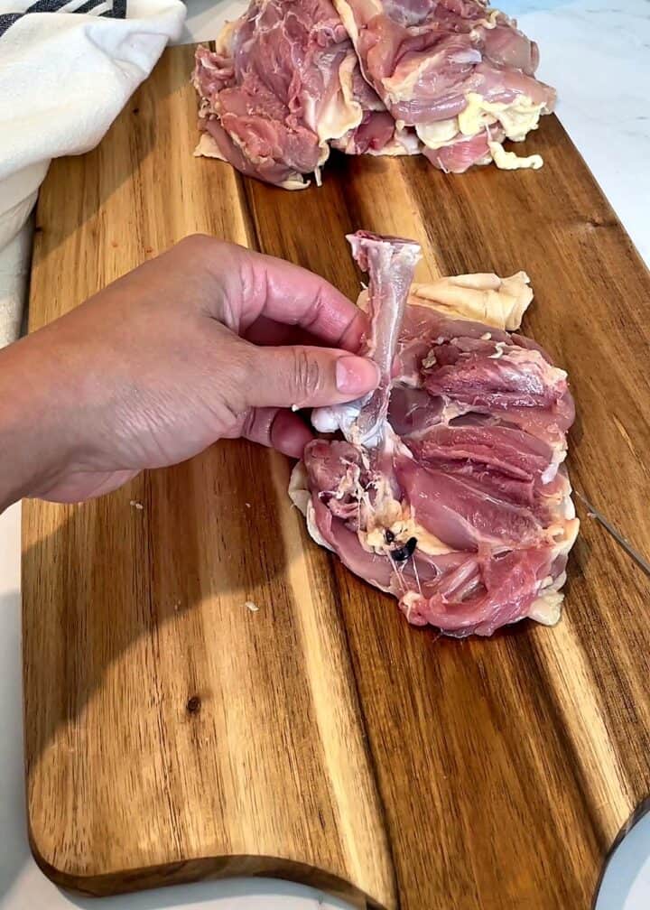 Hand lifting the loosened bone up and away from the opened chicken thigh