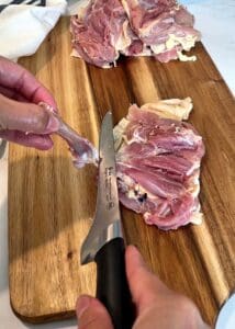 Boning knife cutting through the joint at the knuckle end to release the chicken thigh bone